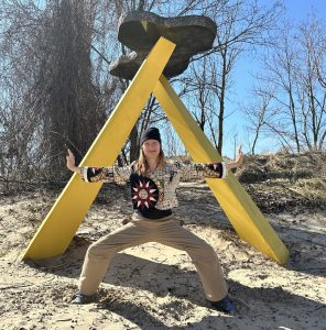Melissa doing Shaolin Standing on a beach in front of yellow triangle.