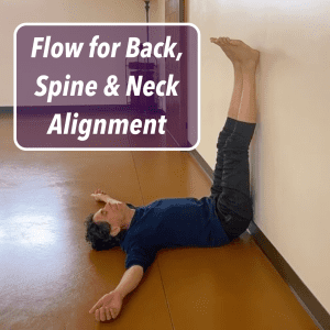 Joe lying on the floor with legs up against a wall, arms relaxed to the sides, demonstrating a gentle inversion pose for back, spine, and neck alignment in a quiet studio space.